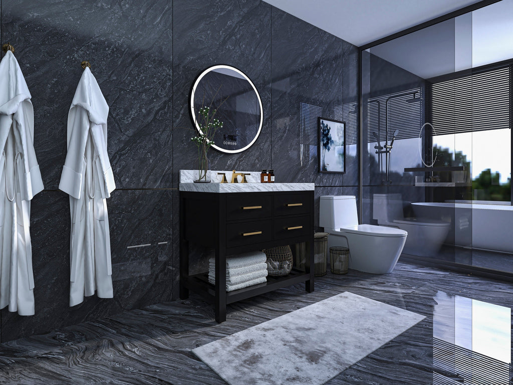 Freestanding black solid wood 36-inch single-sink vanity with a stone marble top, brass faucet and drawer pulls, round illuminated mirror above and folded towels on the lower shelf in a modern stone-walled bathroom.