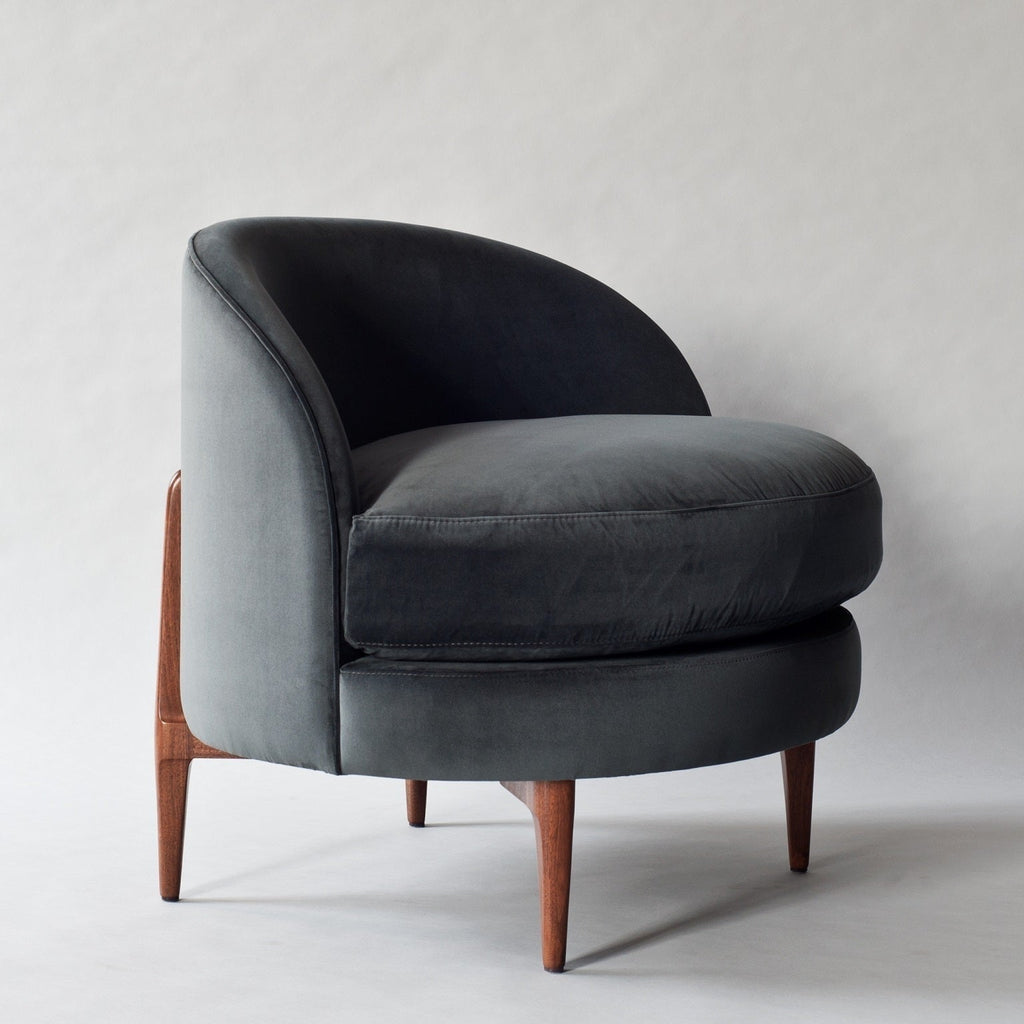 Dark gray velvet accent chair with a curved barrel back, plush rounded seat cushion and exposed solid wood tapered legs.