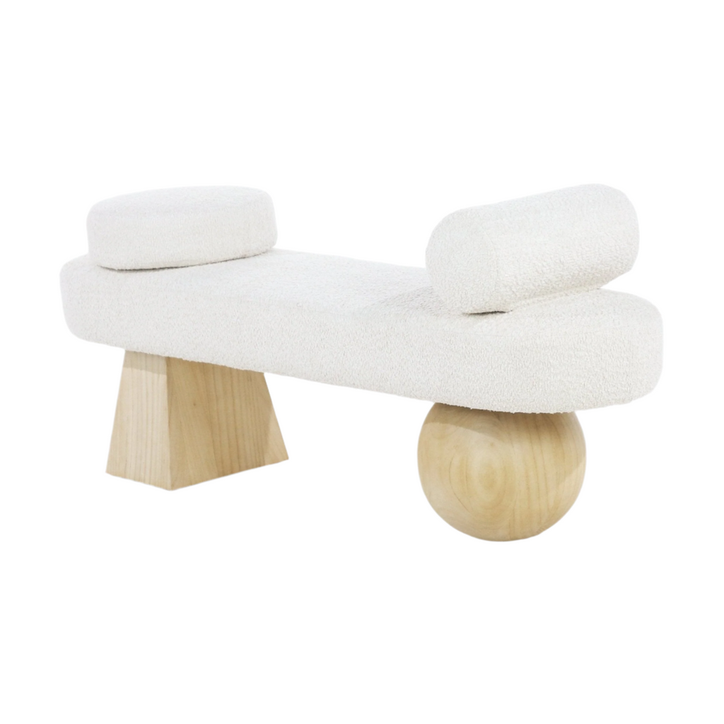 Backless end-of-bed bench upholstered in white boucle fabric with two cylindrical bolster cushions and asymmetrical natural wood legs, a tapered block on one side and a round ball on the other.