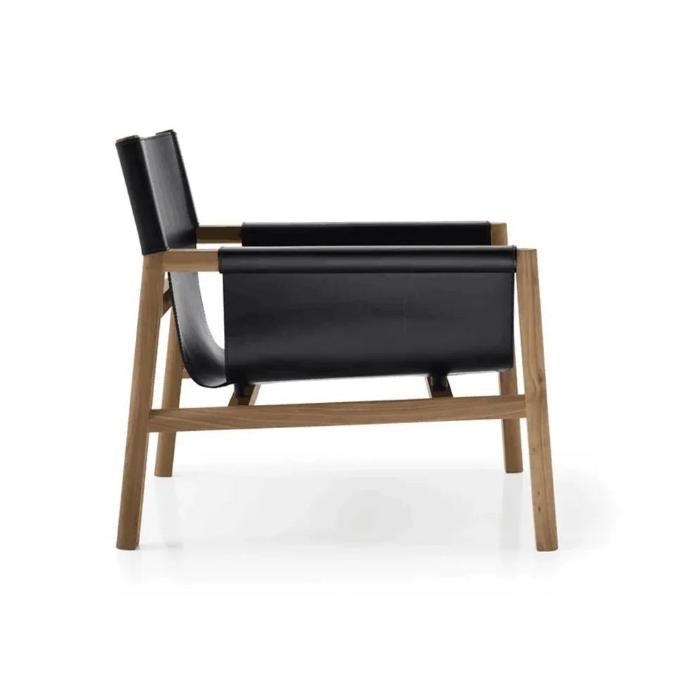 Side view of a mid-century modern accent lounge chair with a natural teak wood frame and black leather sling seat and backrest, showing angled legs and exposed joinery on a white background.