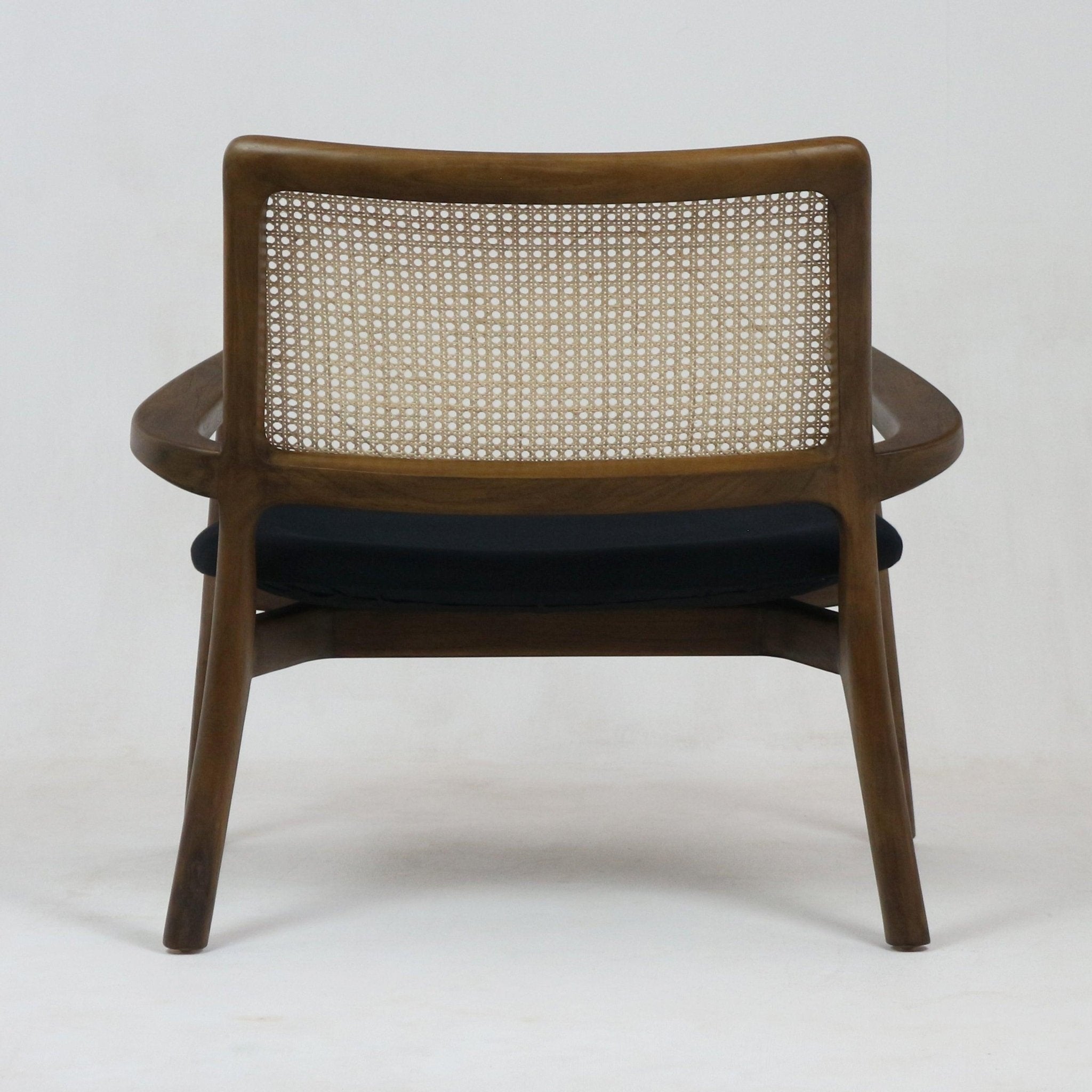 Rear view of a mid-century modern teak lounge chair with a woven cane back and a black upholstered seat cushion on a plain white background.