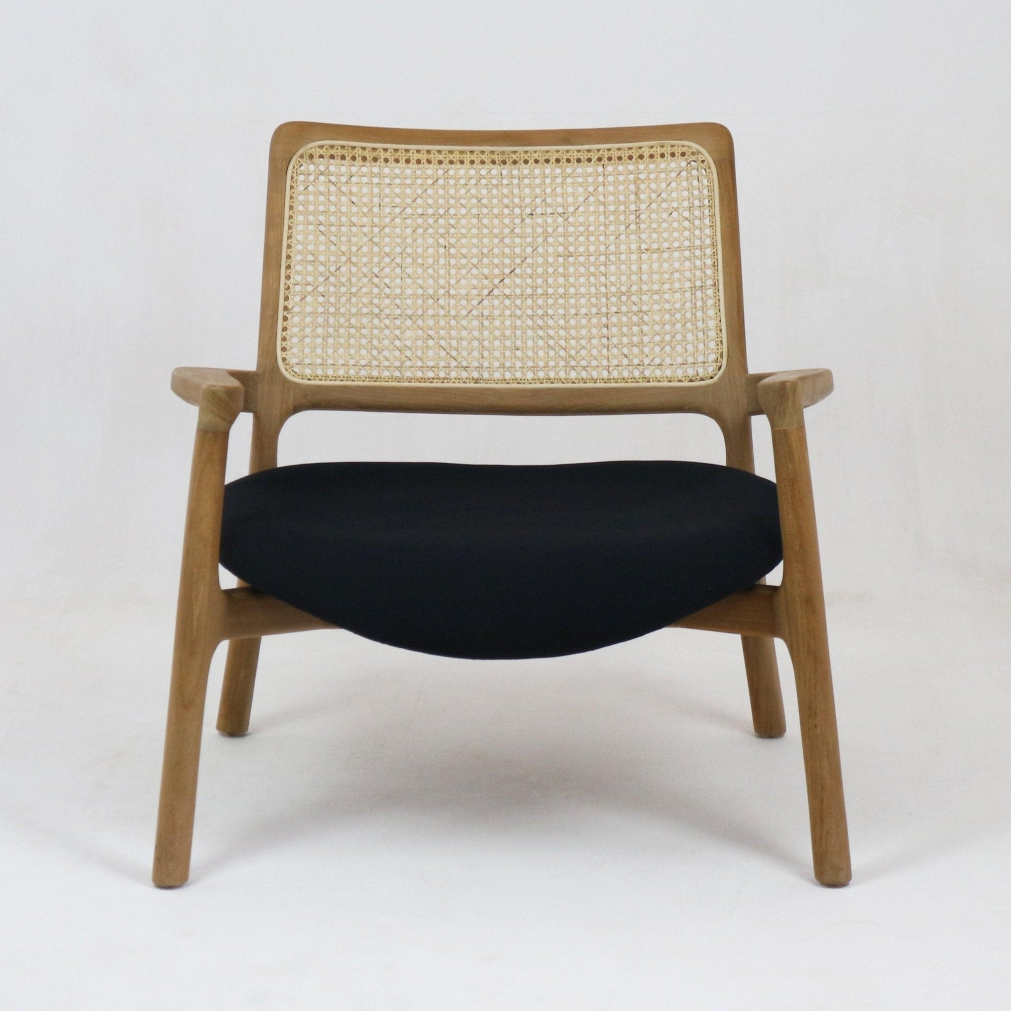 Mid-century modern lounge chair with a teak wood frame, woven cane backrest, slim wooden arms and a low black fabric upholstered seat shown front-facing on a plain white background.
