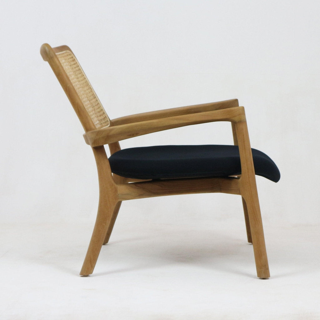 Side view of a teak mid-century modern lounge chair with a woven cane back, sculpted solid wood frame, tapered legs and a dark fabric seat cushion.