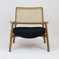Mid-century modern lounge chair with a teak wood frame, woven cane backrest, slim wooden arms and a low black fabric upholstered seat shown front-facing on a plain white background.