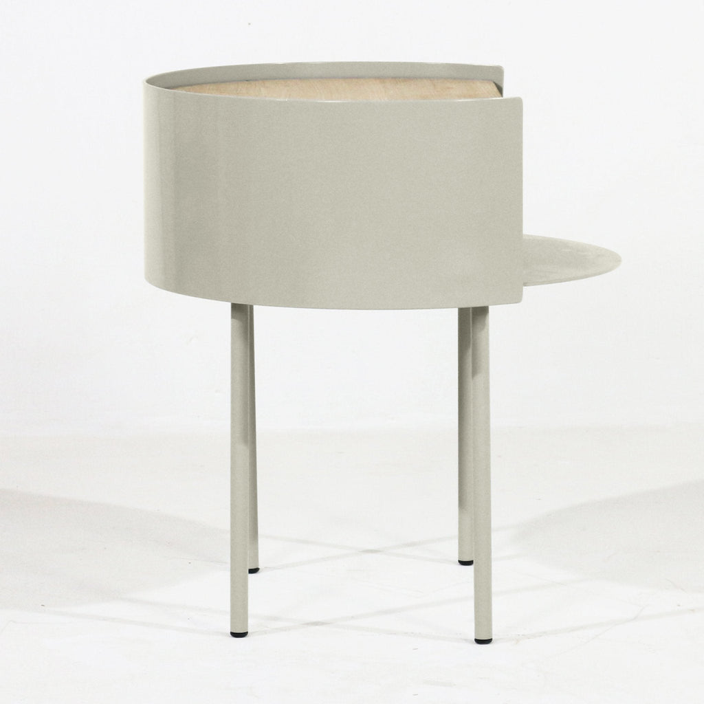 Modern nightstand featuring a curved light gray steel shell with a white oak top visible through the opening, three slim steel legs and a small round side shelf.