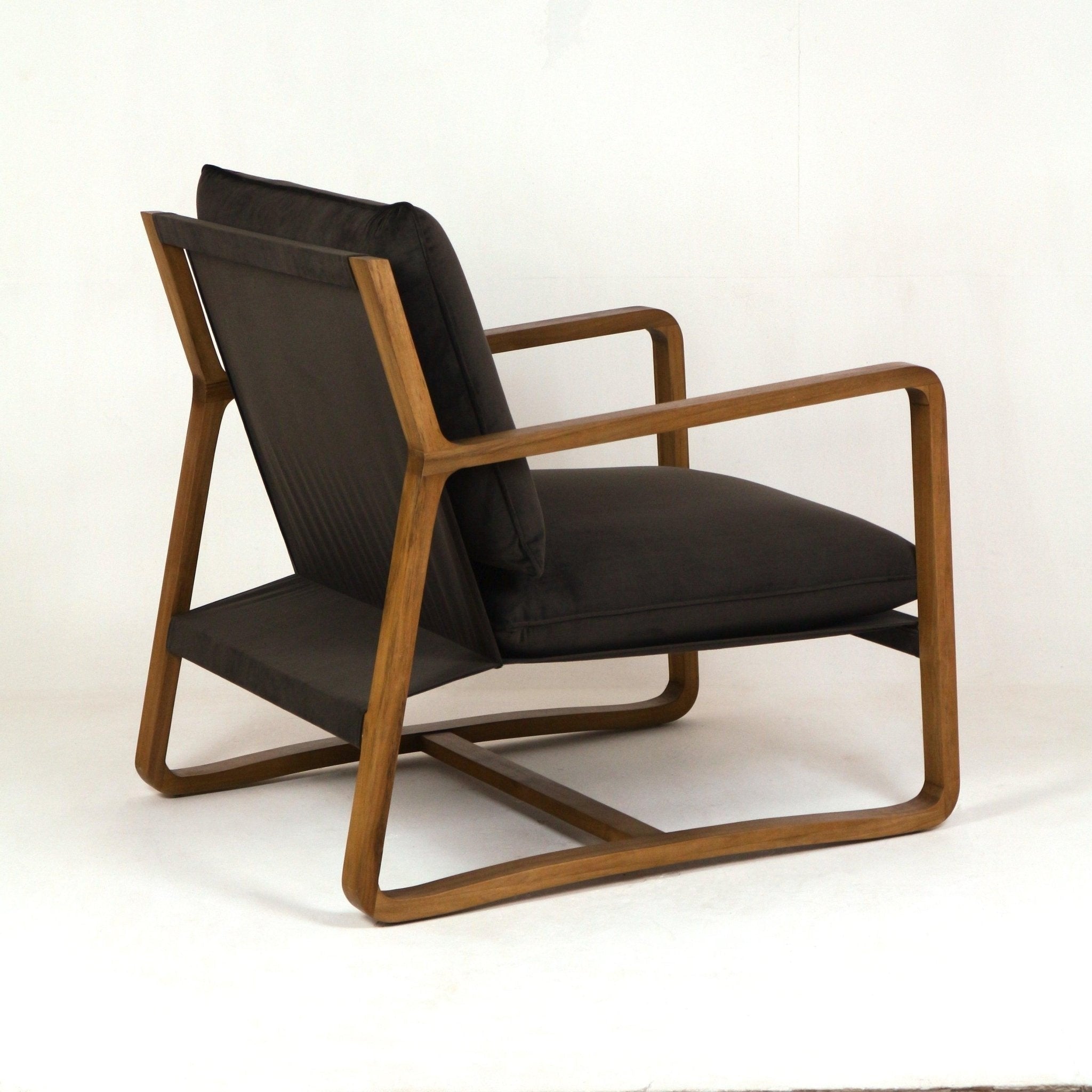 Three-quarter side view of a mid-century modern oak lounge chair with olive-green velvet upholstery, plush seat and back cushions, and a curved solid wood sled frame with open armrests.