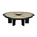 Low round coffee table with a black wood frame and six radial natural cane panels, a central circular opening, and chunky short black block legs in a modern midcentury-inspired style.