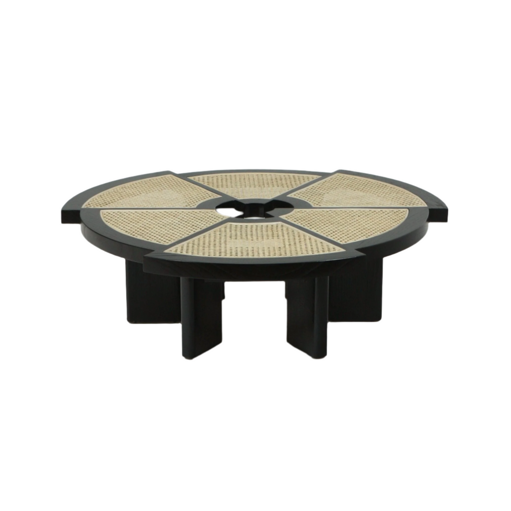 Low round modern coffee table with a black wooden frame and natural cane insets arranged in segmented triangular panels around a small central opening, supported by a sculptural geometric pedestal base.