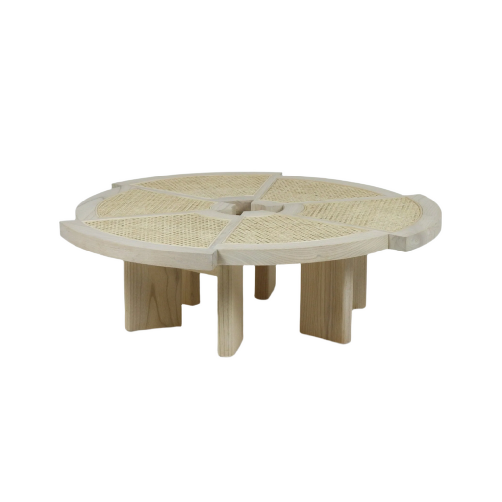 Low round coffee table in natural wood with woven cane inset panels arranged in six pie-shaped sections, thick notched legs and a shallow recessed center for a modern, minimalist living room look.