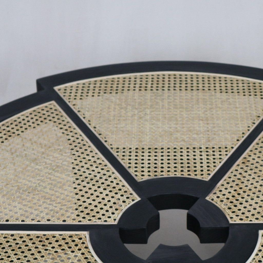 Close-up of a round coffee table top with natural cane weave panels set into a black wooden frame, showing the segmented radial pattern and circular center detail.