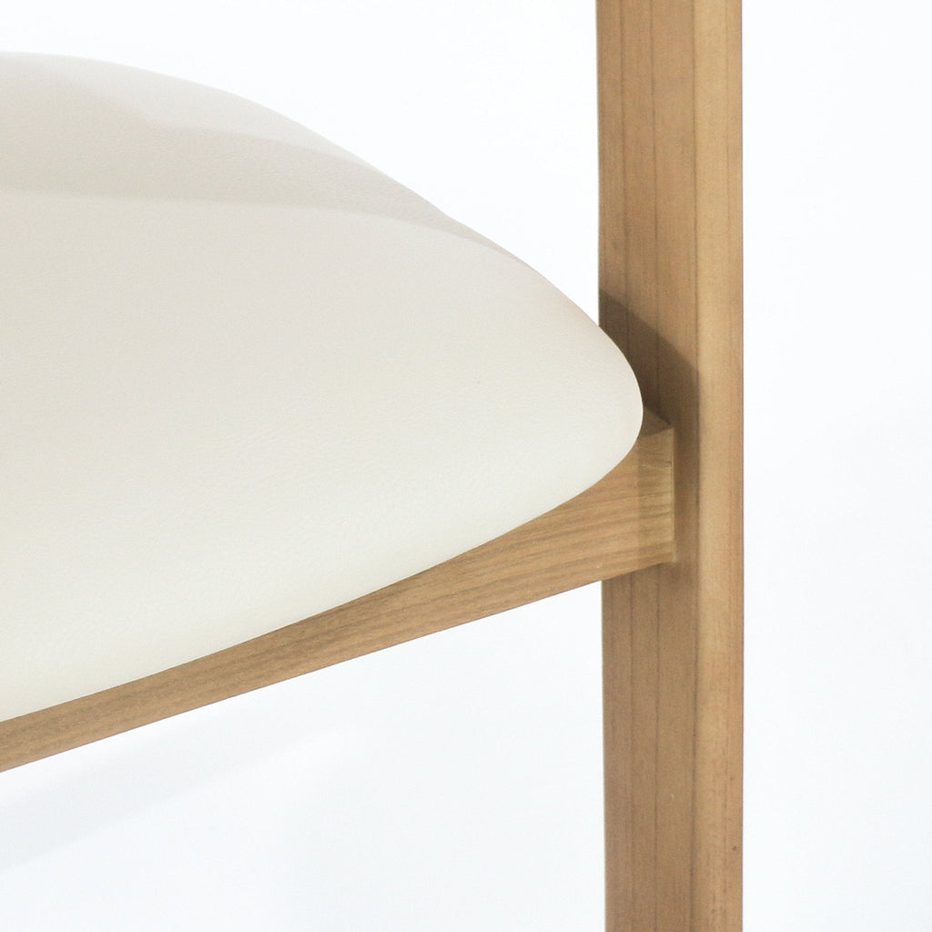 Close-up of a beige leather upholstered dining chair seat showing the rounded cushion edge and the natural teak wood frame and vertical leg with visible wood grain.