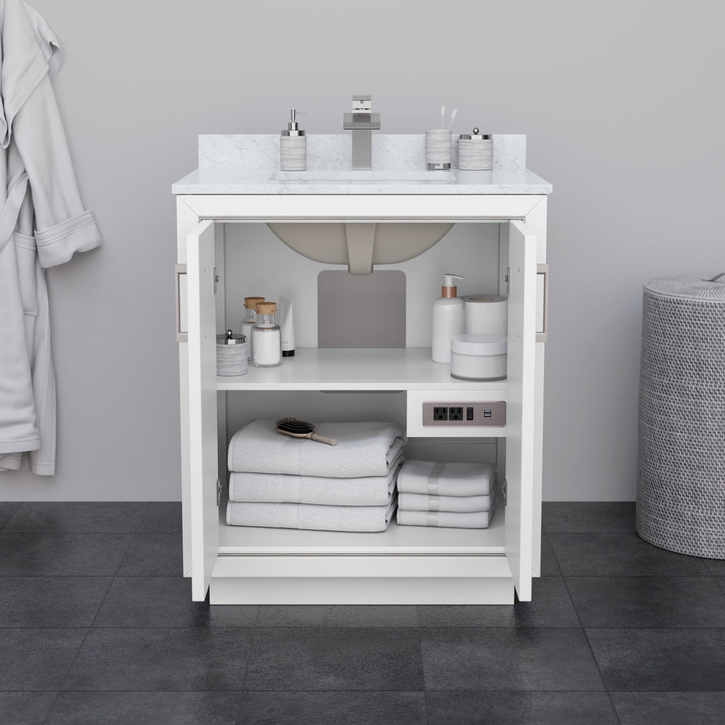Front view of a 30-inch modern white solid wood bathroom vanity with a light stone countertop and integrated sink; open cabinet doors reveal shelves with folded white towels, toiletries, a hairbrush and a built-in power outlet.