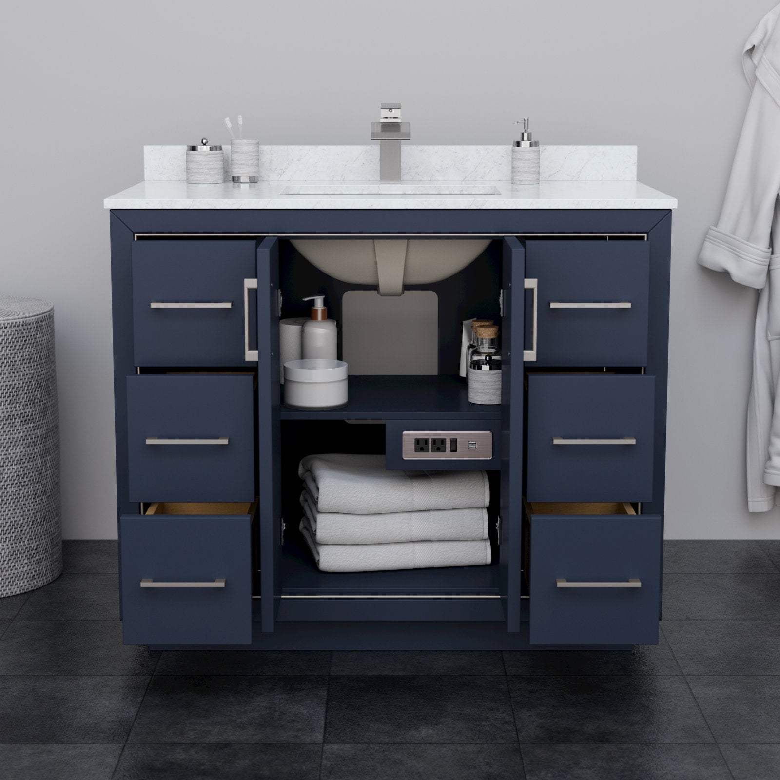 Modern 42-inch solid wood bathroom vanity with white stone countertop and integrated rectangular sink, navy cabinet with brushed-nickel bar pulls, six drawers and open center storage showing towels, toiletries and a built-in outlet.