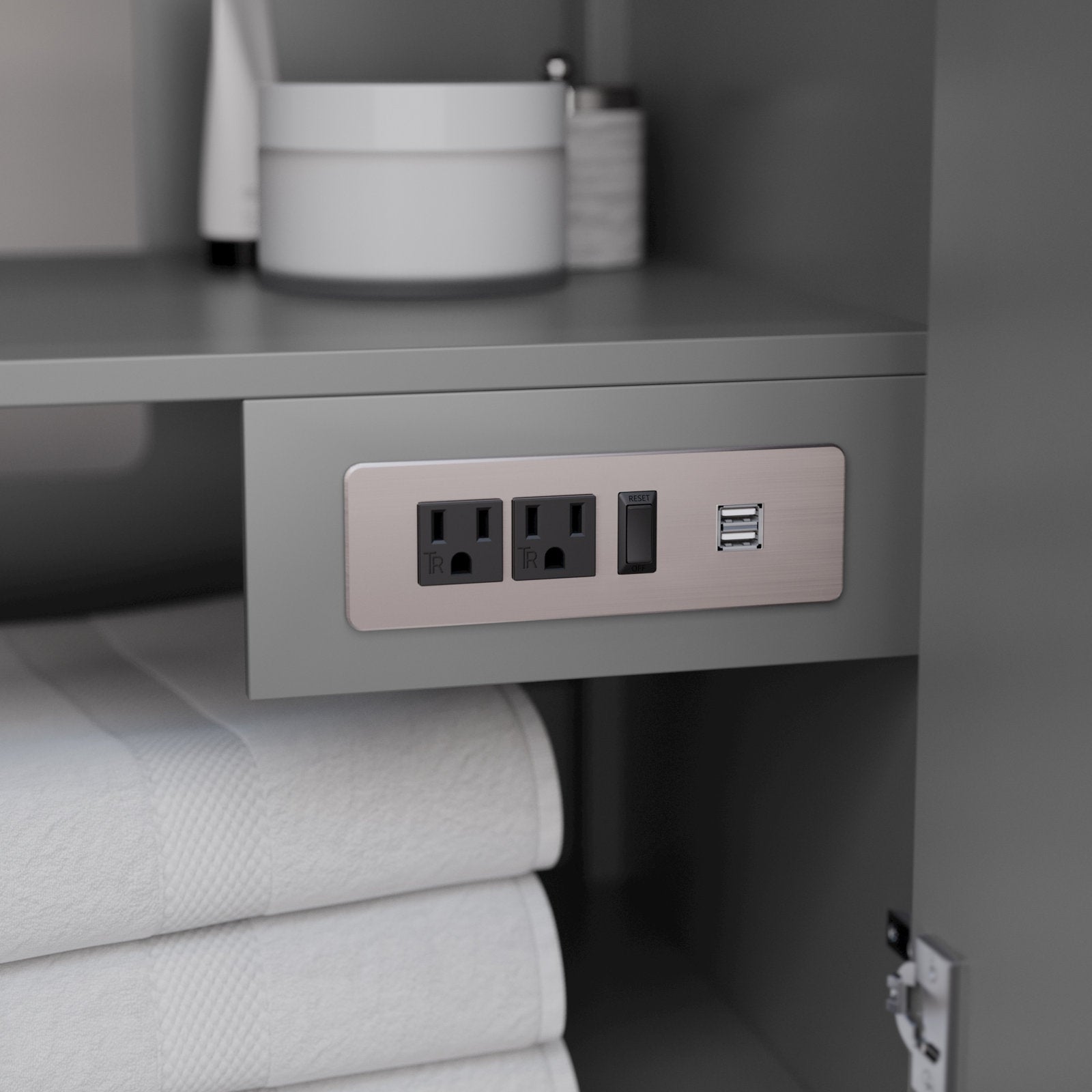Close-up of a stone-finish solid wood vanity interior showing a built-in brushed metal power plate with two grounded outlets, a reset switch and dual USB ports above neatly folded white towels and toiletry containers.